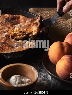 Scatto verticale di una persona che prende un pezzo di a. torta vicino a una ciotola di pesche Foto Stock