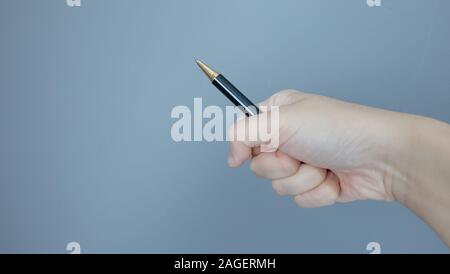 Mano in presa su una penna a sfera e lo si punta verso un angolo, con copia spazio sulla sinistra. Foto Stock