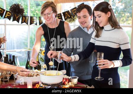 I festaioli intingere il pane in fonduta di formaggio in una vacanza fondue party Foto Stock