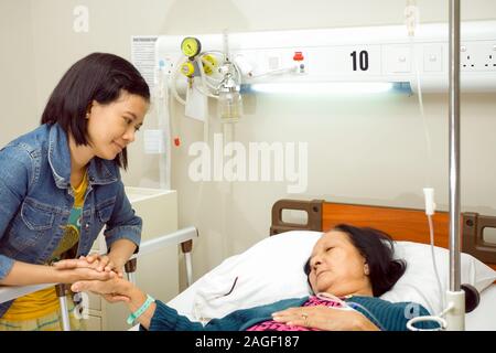 Sud-est asiatico nipote visita a sua nonna malati in ospedale. Tenendo le mani. Foto Stock