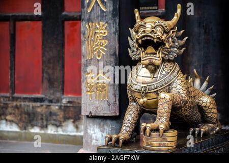 Statua della mistica cinese in ottone dorato custode lion sul muro rosso sfondo nel cortile del buddista di Tempio Wenshu Monastero, Chengdu, Sichua Foto Stock