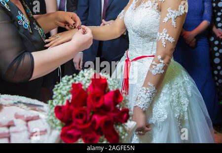 Sposa la messa sui gioielli, focus sul bracciale. Close up di groom dando la sua sposa bracciale come simbolo del suo amore il loro giorno delle nozze. Damigella aiuta a Foto Stock