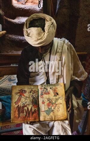 Etiopia, Amhara Region, Lalibela, Arbatu Ensessa, Biblia Chirkos, antiche rocce scavate chiesa, sacerdote mostra 800 anno-vecchio vangelo illuminato Foto Stock