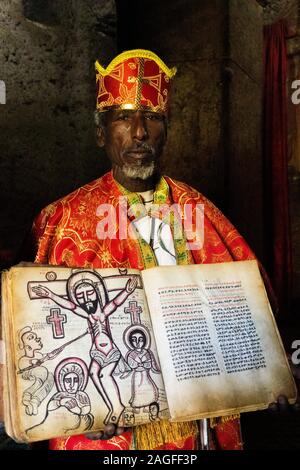 Etiopia, Amhara Region, Lalibela, Arbatu Ensessa, Biblia Chirkos, sacerdote nelle vesti mostra 800 anno-vecchio vangelo illuminato con Crocifissione immagine Foto Stock