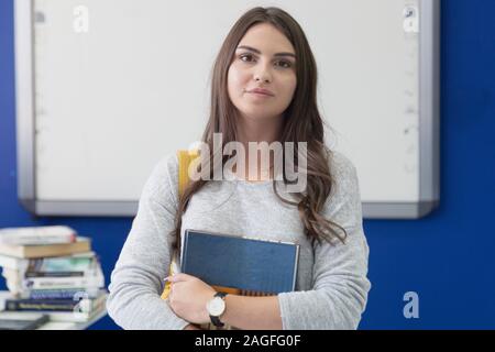 Ritratto di una giovane bella studentessa all interno della classe. Lei tiene libro nelle sue mani durante la classe nella parte anteriore della scheda smart. Foto Stock