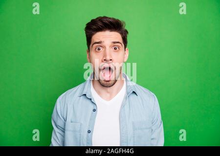 Ritratto di crazy mad spaventato ragazzo gridando con terrore vedendo le vendite cessato indossando t-shirt bianco isolato su verde vivido colore di sfondo Foto Stock