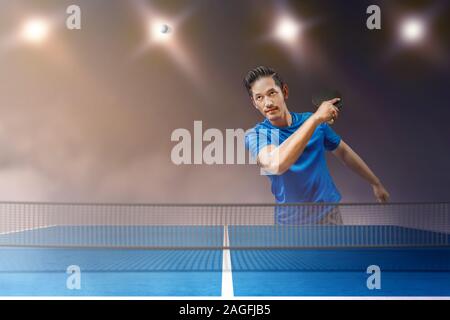 Tabella asiatici giocatore di tennis uomo swing il ping pong racket con faretti sfondo Foto Stock