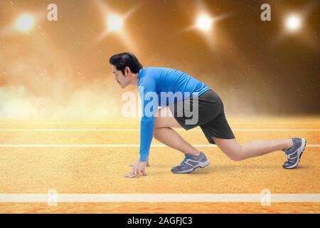 Asian runner uomo pronto a correre sulla pista da corsa con faretti sfondo Foto Stock