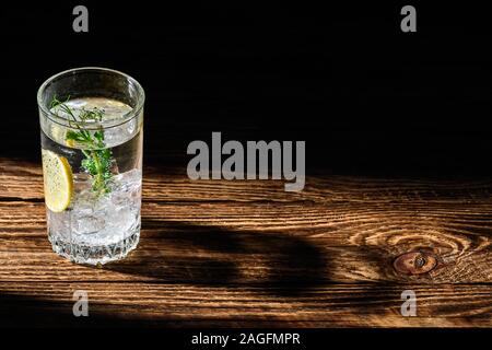 Carbonare acqua fredda con ghiaccio e limone scenda lungo ombra sul tavolo di legno Foto Stock