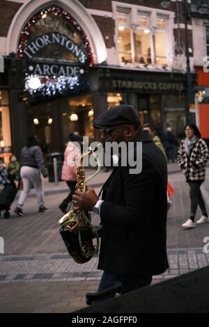 LEEDS, Regno Unito - Dic 07, 2019: un suonatore ambulante a giocare il suo sassofono su Leeds Briggate high street nel corso di una intensa giornata di Natale Foto Stock