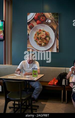 Uomo solo studiando la documentazione in un ristorante interno contro una parete sullo sfondo di arte cibo Foto Stock