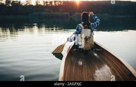 Vista posteriore della donna in canoa sul lago al tramonto Foto Stock