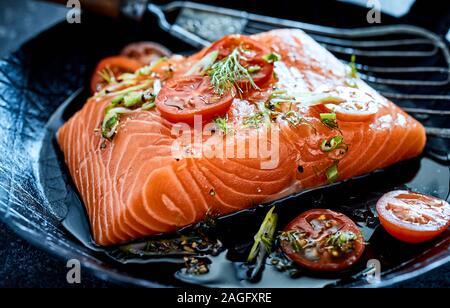 Fresco e salutare raw bistecca di salmone con omega-3 in una padella con olio e tritato fresco assortimento di erbe e pomodori Foto Stock