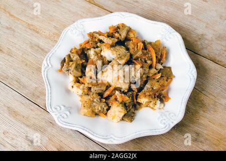Merluzzo bianco Filetto di pesce con la carota e la cipolla marinata su una piastra bianca su un naturale in legno rustico sfondo. Selective soft focus. Copia di testo spazio. Egli Foto Stock