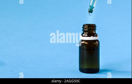 Close-up, cosmetici, bottiglia di vetro con una pipetta e acido ialuronico su uno sfondo blu Foto Stock