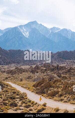 Donna in abito giallo a piedi attraverso Alabama Hills, in California, Stati Uniti d'America Foto Stock