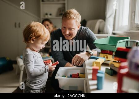 Padre guardando figlio giocare con blocchi giocattolo in salotto Foto Stock