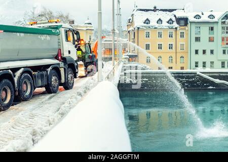 Pesante servizi municipali Macchine rimozione neve da strade di città. Grande trattore spalaneve soffiando la neve da bridge road nel fiume. Pulizia di strade Foto Stock