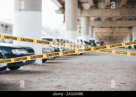 Grande area. Spia gialla di attenzione nastro in prossimità del parcheggio auto al giorno. Scena del crimine Foto Stock