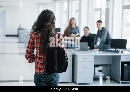 Vista dal retro. Un gruppo di giovani in abiti casual lavorando nell'ufficio moderno Foto Stock
