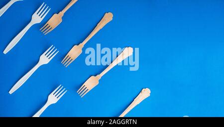 Bambù organico forcelle monouso vs quelli in plastica alla moda su sfondo blu. Ecocompatibili e di legno non-oragnic plasticforks Foto Stock