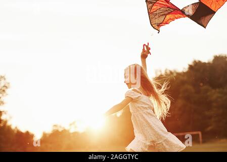 Bella foresta dietro. Felice ragazza in bianche vesti divertirsi con il kite in campo. La bellissima natura Foto Stock