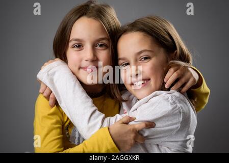 Gemello ragazze sorelle sono in posa per la fotocamera. Felice gemelle guardando la telecamera, ridendo, sorridente, avvolgente, tenendo le mani. Professio Foto Stock