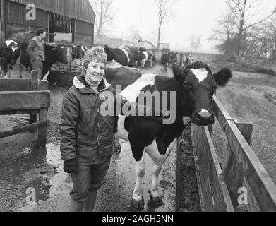 1980s, storico, signora contadina con il suo bestiame in un cortile, Yorkshire, Inghilterra, Regno Unito. Foto Stock