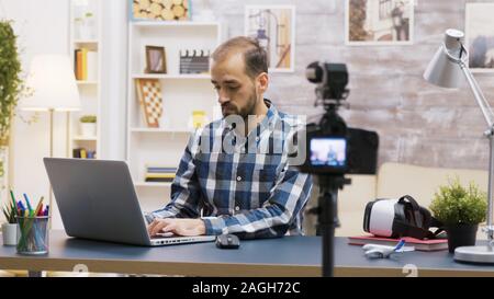 Famoso giovane vlogger digitando su laptop mentre parla con i suoi abbonati su un podcast. Contenuto creativo creatore. Foto Stock