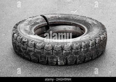 Vecchio danneggiato utilizzato usurati carrello pneumatico poggia su una strada asfaltata Foto Stock