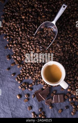 Caffè torrefatto in grani, e una tazza di caffè espresso con una vista da sopra su uno sfondo scuro Foto Stock