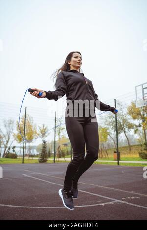 Active longhaired brunette girl salta su-salto corda Foto Stock