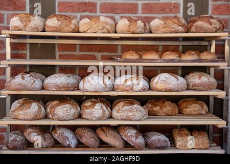 Prodotti da forno. Una varietà di pani appena sfornati in scaffalature in legno di un paese panificio di fronte a un muro di mattoni. Concetto di nutrizione sana. Foto Stock