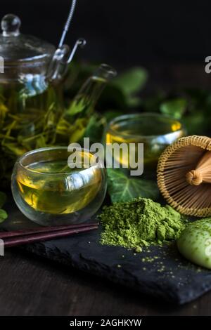 Giapponese del tè tradizionale matcha e sencha nella teiera in vetro con bambù mescolando con una frusta per dolci e torte di riso mochi Foto Stock