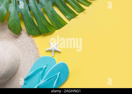 Spiaggia femmina cappello di paglia, vestito, flip-flop, monstera tropicale su giallo. Vista dall'alto. Estate concetto di viaggio. Vista superiore e spazio per il testo. Foto Stock