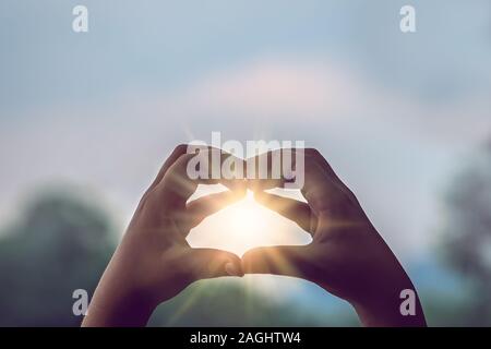 Womans mani cattura la luce solare sunray mentre messa a forma di cuore Foto Stock