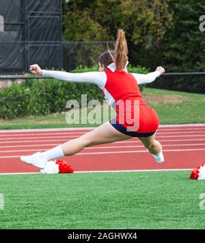 Un high school cheerleader adolescente in un rosso e bianco uniforme è saltare in aria la sua pratica di routine prima della sua performance. Foto Stock