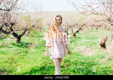 Bionda in abito rosa passeggiate nel giardino con alberi in fiore Foto Stock