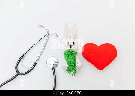 Semplicemente minimal design toy bunny cuore rosso e apparecchiature di medicina uno stetoscopio isolati su sfondo bianco. La cura della salute dei bambini concetto medico. Pediatra simbolo. Flat Top laici visualizza lo spazio di copia Foto Stock