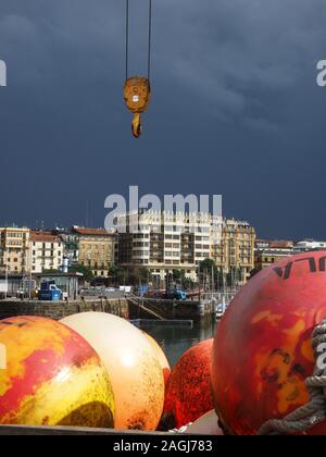 Sole su boe luminose con puleggia gru nel cielo scuro di imminente tempesta oltre il piacere marina nella baia di San Sebastian, nel nord della Spagna, Europa Foto Stock