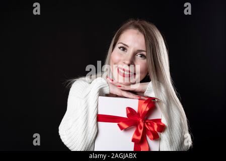 Ritratto in studio di sorridere giovane bella donna detiene confezione regalo rossa. Isolato su sfondo nero. Foto Stock