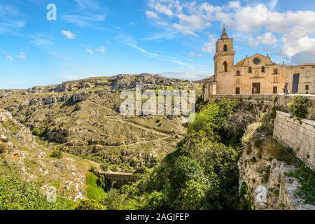 Percorsi da antiche grotte dei sassi tagliati giù per il pendio della montagna e nel canyon in Matera, Italia, come il San Pietro Caveoso chiesa sorge sulla cima di una scogliera Foto Stock