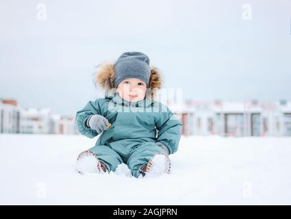 Carino baby boy in menta Tuta invernale seduti sulla neve all'aperto Foto Stock