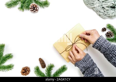 Natale composizione d'inverno. Donna mani di incarto regali di Natale scatola con coni di pino, abete rami su sfondo bianco. Appartamento laico, vista dall'alto, copia spa Foto Stock