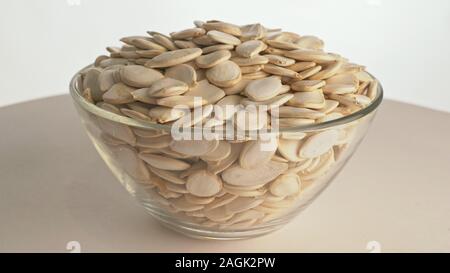 I dadi con la buccia semi di zucca sono ruotare su di una tavola in una piastra. Snack nel piatto trasparente isolato su un sfondo bianco sono la filatura in movimento. Foto Stock