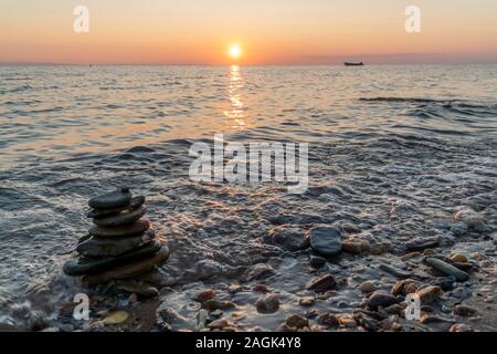 Pila di roccia sulla spiaggia durante il tramonto, con una barca in background. Zen concetto dell'umore. Foto Stock