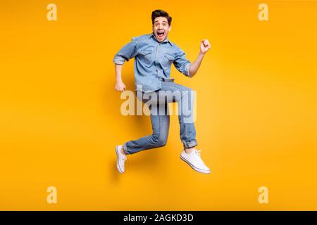 Girato a lunghezza piena dimensione del corpo foto di allegro positivo uomo pazzo urgente per vendite e convenienti in bianco sneakers denim isolato colori vividi Foto Stock