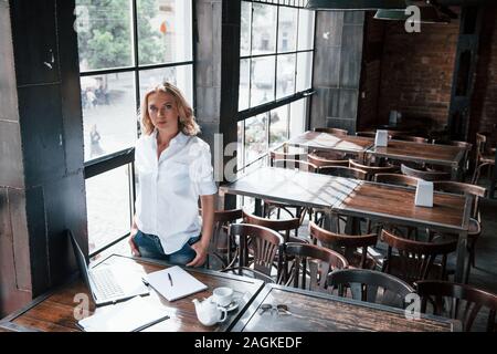 Aspetto fiducioso. Imprenditrice con ricci capelli biondi in ambienti interni in cafe di giorno Foto Stock
