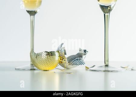 Due rotture di giallo e grigio palle di Natale e un paio di occhiali con champagne su un tavolo bianco. Il concetto di disfacimento e di conflitto familiare Foto Stock