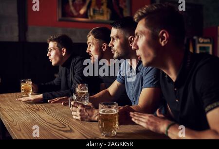 Tre gli appassionati di sport in un bar di guardare partite di calcio. Con la birra in mano Foto Stock